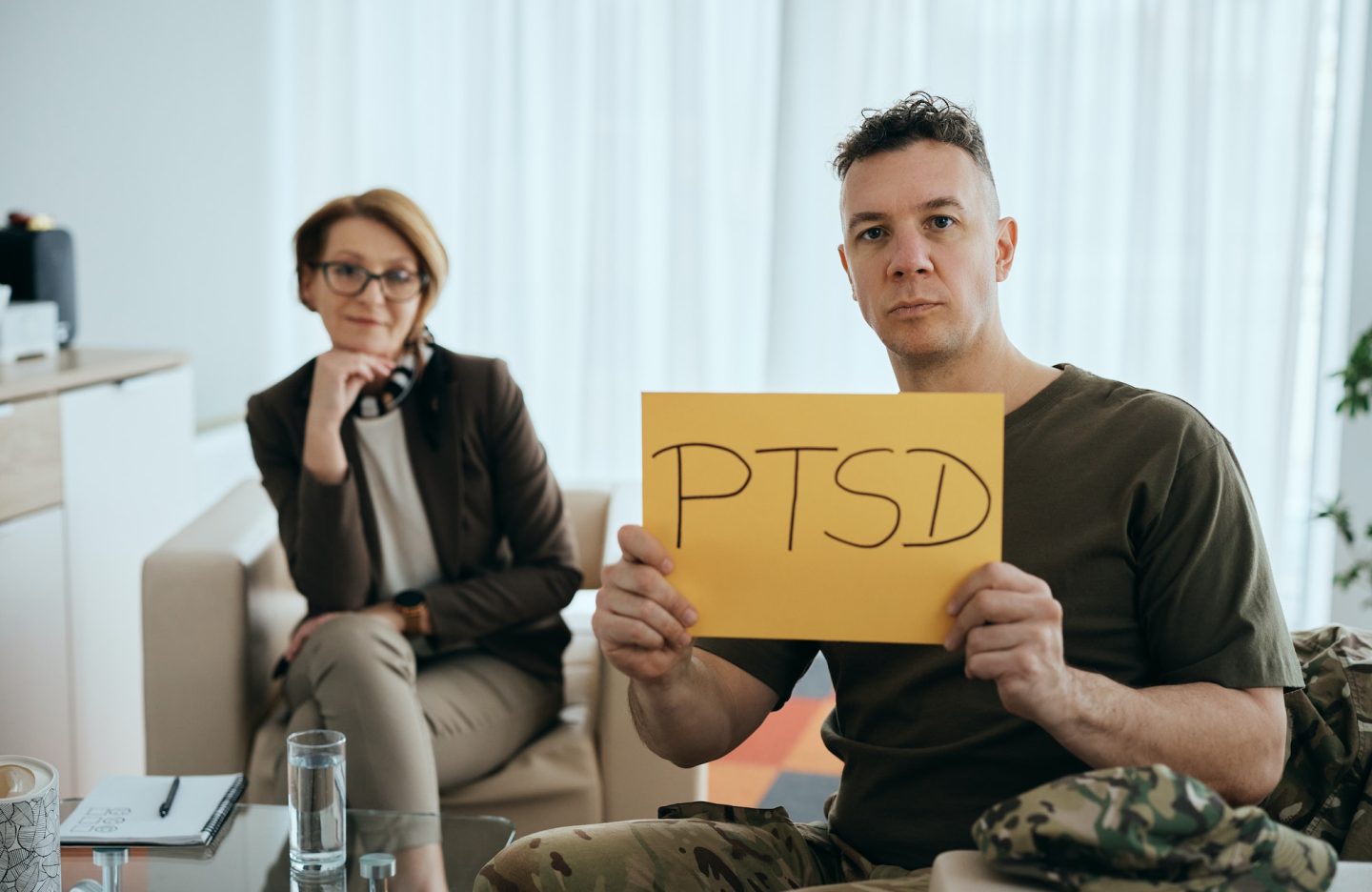 Soldier holding placard with PTSD message during counseling with psychiatrist and looking at camera.